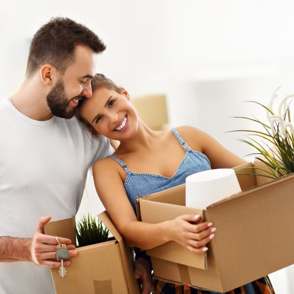 man and woman smiling, hugging, and holding moving boxes with key to new home