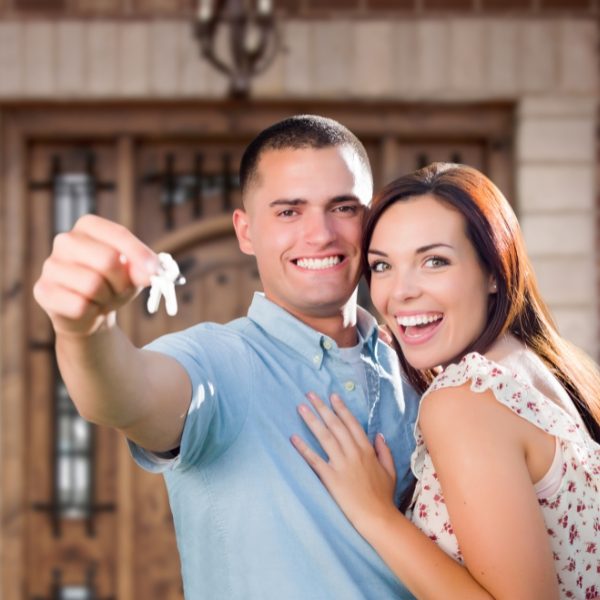happy smiling couple holding new home keys up, in front new house they are moving into/ move in/out cleaning services